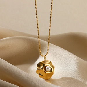 Detailed macro view of an 18K gold textured ball pendant with a white pearl inlay