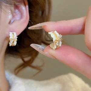 Detail view of 18k gold plated C-shaped earrings with rhinestones and white bow