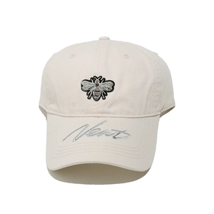 Close-up of cream baseball cap with bee embroidery and silver script on the brim