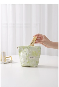 Detailed shot of a light green floral makeup bag with gold zipper and beige brand tag