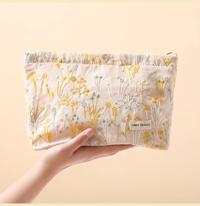 Close-up of floral plant embroidery on beige canvas makeup bag with hand holding detail