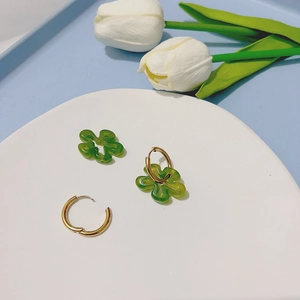 Détail de créoles dorées avec pendentifs fleurs en résine verte sur un plateau blanc