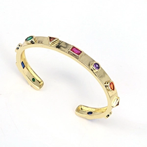 Detail of gold open cuff bracelet with colorful geometric zircons on white background