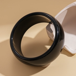Close-up of a wide glossy black acrylic cuff bracelet on a minimalist beige background
