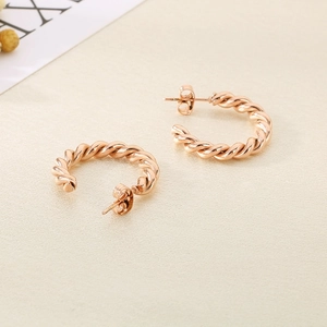Détail des boucles d'oreilles torsadées en forme de C en or rose sur tissu texturé