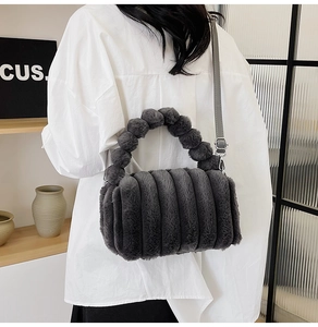Detail of dark grey plush handbag with fur ball handle and adjustable strap worn by model