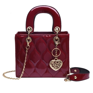 Detail of red patent leather handbag featuring wave stitching and gold heart charm