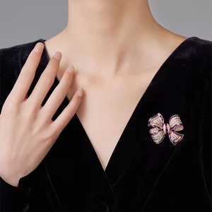 Elegant purple and gold bow brooch with crystals on a black V-neck top detail view