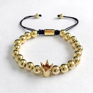 Close-up of golden beaded bracelet with crown charm and adjustable black braided cord