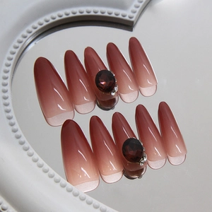 Red almond press-on nails with ruby rhinestones and cat eye gradient on a mirror