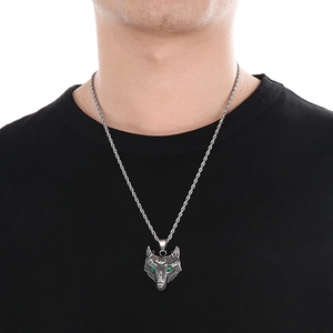 Detailed shot of a silver wolf head pendant with green eyes worn on a black shirt