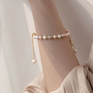 Detail of adjustable pearl bracelet with zircon flower charm and golden beads finish
