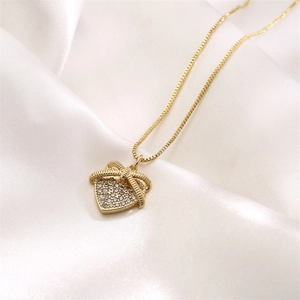 Dettaglio della collana a cuore dorata con fiocco e zirconi su seta bianca