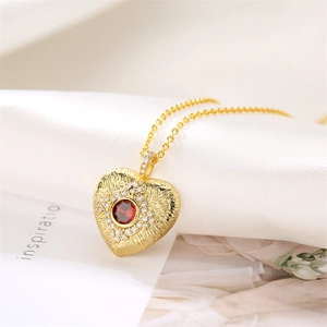Macro shot of gold heart pendant with red round gemstone and sparkling small diamonds