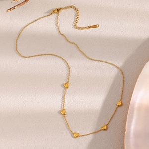 Detailed macro view of gold plated stainless steel heart charm necklace on beige surface