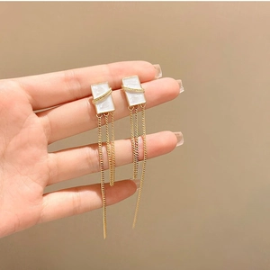 Detail of long gold tassel earrings with white shell texture inlays held by hand