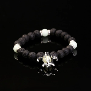Black volcanic stone beaded bracelet with luminous turtle charm on reflective surface
