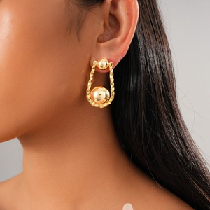 Pendientes de bolas de metal chapados en oro 18K en modelo con fondo gris neutro