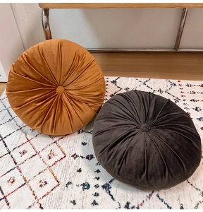 Close-up of pleated velvet pumpkin cushions in orange and brown on a textured rug