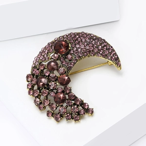 Macro shot of gold crescent moon brooch with inlaid purple rhinestones on white display