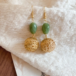Détail macro de boucles d'oreilles dorées avec perles en résine verte sur tissu texturé