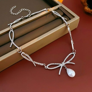 Détail d'un collier nœud argenté orné de strass avec un pendentif perle en goutte