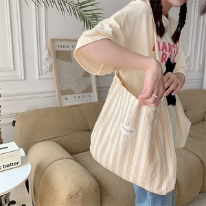 Detail shot of stylish striped canvas tote bag with studio label on a casual model shoulder