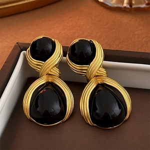 Close-up of gold metal earrings with black teardrop acrylic stones in a jewelry box