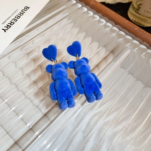 Detail view of blue flocked heart and bear earrings on a luxury glass tray background