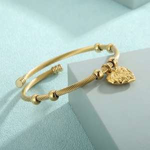 Detail of gold twisted cable cuff bracelet with leaf pendant and bead on a blue background