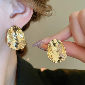 Golden irregular geometric stud earrings with hammered texture on a model's ear
