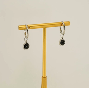 Détail de boucles d'oreilles argentées avec pierre noire polie sur un support doré
