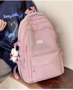 Detail of pink nylon school backpack with a cute white dog plush pendant and multi-compartments