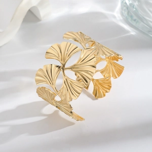 Macro shot of gold ginkgo leaf cuff bracelet showing intricate hollow design and metal texture