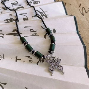 Detailed view of silver butterfly pendant with green ceramic beads on Chinese fan