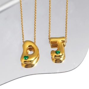 Detail view of 18k gold plated bubble pendants with green heart stones on a mirror surface