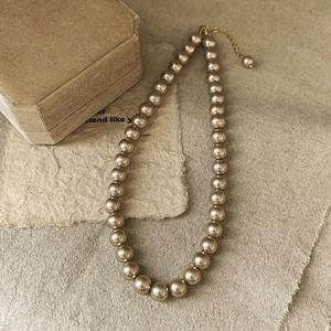 Detailed view of vintage champagne pearl necklace with adjustable gold clasp on linen
