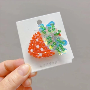Détail d'une pince à cheveux perlée à la main avec perles rouges et paillettes vertes