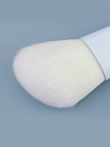 Macro view of dense white synthetic bristles on a blue gradient makeup brush head