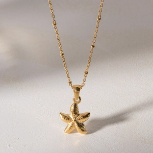 Elegant gold starfish pendant necklace with beaded chain on a minimalist white background