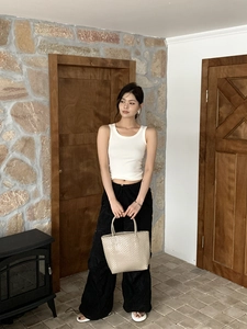 Front view of model carrying a beige woven tote bag with white top and black wide trousers