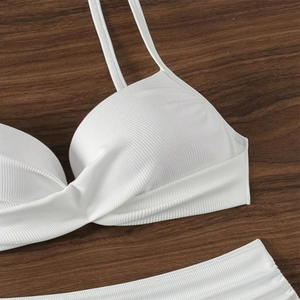 Detailed view of white ribbed bikini fabric with thin straps on dark wooden surface