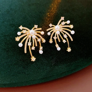 Detail of 18K gold fireworks pearl earrings with sparkling zircons on green velvet