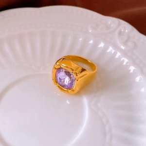 Macro detail of gold plated ring with large faceted purple zircon on white ceramic tray
