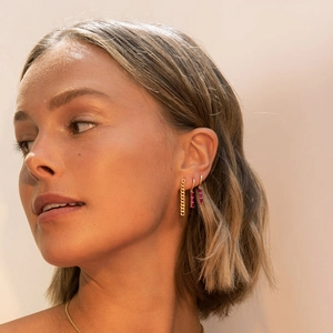 Close-up of elegant gold chain earrings and red rectangle gemstone studs on model