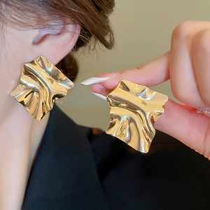 Detailed view of oversized irregular gold fold earrings with metallic texture