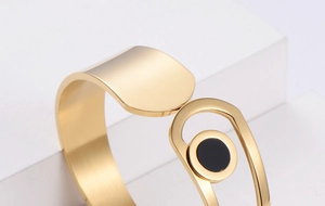 Macro shot of gold cuff bracelet featuring brushed finish and black circular element