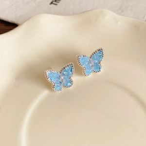 Detail of asymmetrical light blue butterfly earrings with crystals and fringe in a dish