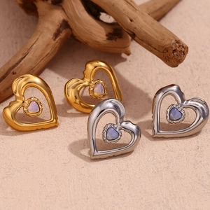 Macro detail of gold and silver heart studs with iridescent opal stones on a beige surface