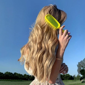 Yellow hollow-out hairbrush for detangling long wavy hair outdoors in daylight